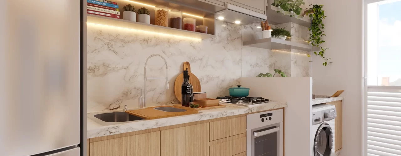 Cozinha compacta planejada com bancada e backsplash em mármore, armários superiores bege e inferiores de madeira clara, cooktop com forno embutido e área de serviço integrada com máquina de lavar, iluminada por luz natural vinda da porta‑janela.